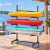 Black metal 3-tier kayak storage rack with wheels, holding colorful kayaks on a dock, for outdoor boat organization.