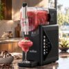 Norda black plastic/metal slushie machine with clear tank, dispensing a red frozen drink into a glass.