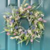 Artificial spring wreath with colorful daisies, lavender, and greenery on a teal door, for home decor.