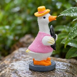 Resin duck garden statue, white with pink shirt, yellow hat, orange beak/feet, holding black umbrella. Outdoor decor.