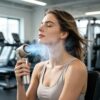 Portable misting fan, gray plastic and silver metal, cooling a woman's face at the gym.
