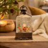 Bronze-finish resin and glass Christmas lantern snow globe with Santa, tree, and gifts, for festive home decor.