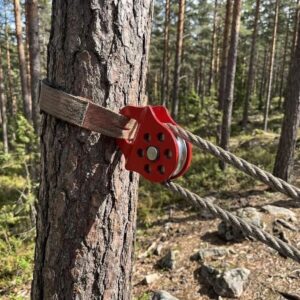 Red metal tree-mounted pulley block with single silver wheel and multiple holes, used with a strap and wire rope.