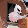 Inflatable white ghost Halloween decoration with red eyes, black mouth, and pink internal lighting, emerging from a wind