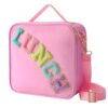 Pink nylon lunch bag with colorful chenille "LUNCH" patch, gold hardware, top handle, and adjustable shoulder strap.