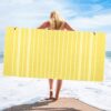 Yellow cotton beach towel with white stripes and tassels, held by woman on sandy beach.