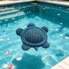 Blue mesh turtle-shaped pool cleaner floating in a swimming pool with flower petals.