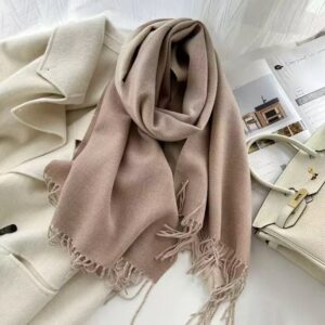 Soft Beige Cashmere Scarf With Fringe, Draped Over A Cream Coat, For Elegant Winter Warmth.