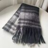 Soft fuzzy black and grey plaid wool scarf with fringe, folded on a white table for warmth and style.