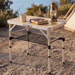 Portable folding camping table with light wood-look top, aluminum frame, and black mesh storage for outdoor use.